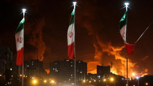 Foto: Bendera Iran berkibar saat api dan asap dari serangan Israel terhadap depot minyak Sharan membubung, menyusul serangan Israel terhadap Iran, di Teheran, Iran, 15 Juni 2025. (via REUTERS/Majid Asgaripour)